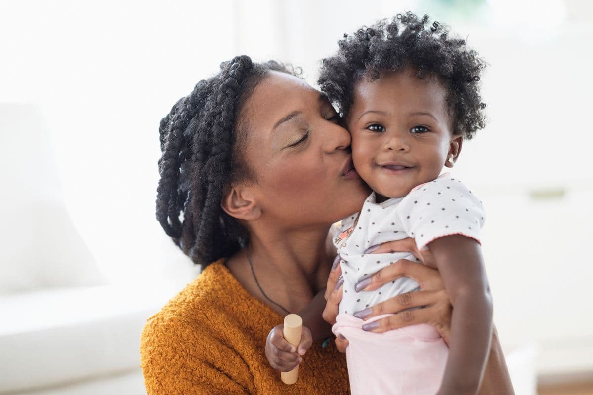 A mother kissing the cheek of her smiling toddler