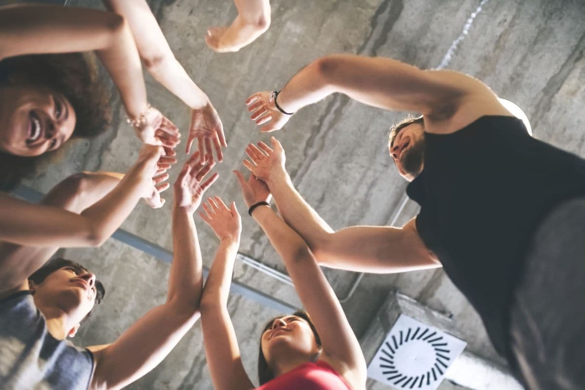 A group of young people joining hands in a circle, seen from below