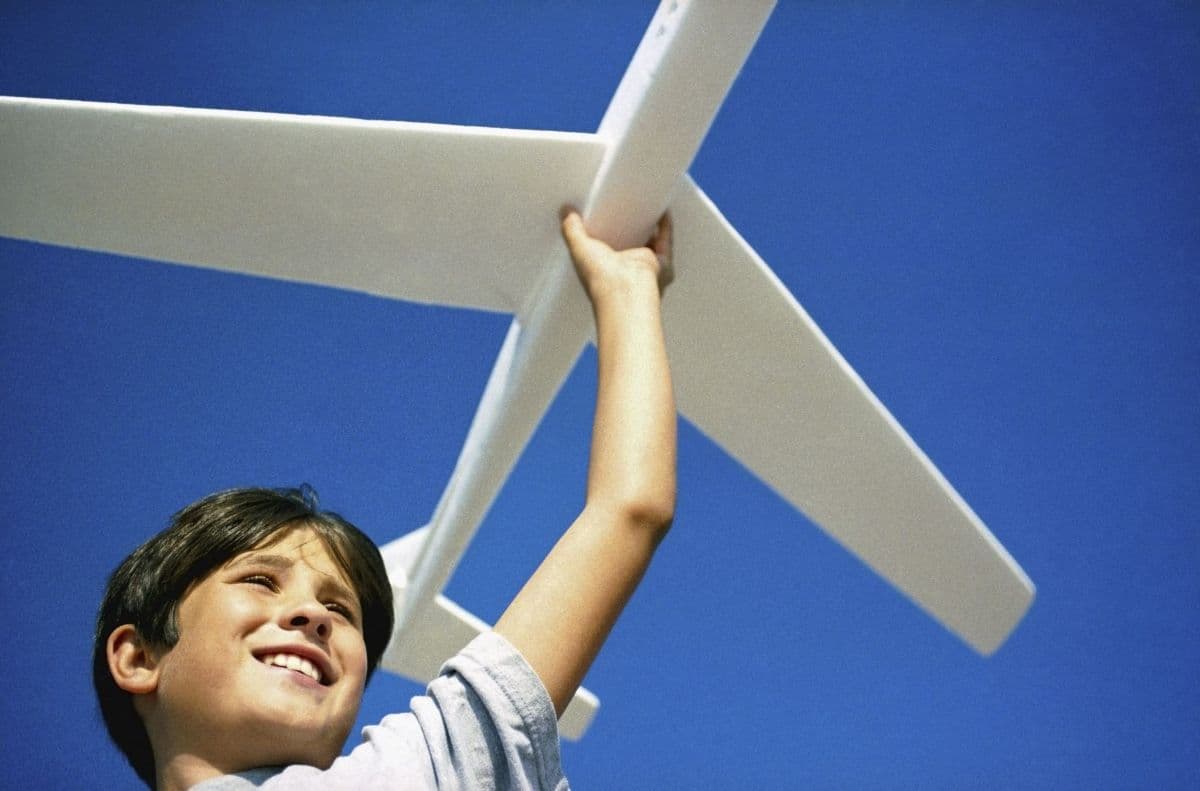 A smiling boy holding a large model aeroplane up against a blue sky